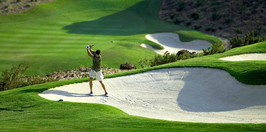 Championship Golf Courses Man trying to hit out of a sand trap on a lush green golf course